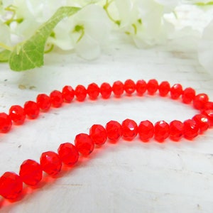 May include: A strand of red faceted glass beads. The beads are strung on a clear thread and are arranged in a circular shape.