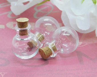 May include: Three clear glass bottles with cork stoppers. The bottles are round and have a small opening at the top. The bottles are sitting on a pink surface.