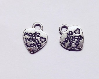 Puede incluir: Dos abalorios de plata en forma de corazón con un bucle para sujetarlos a un collar o pulsera. Los abalorios tienen la inscripción "Made with Love".