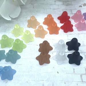May include: Assortment of 18 translucent flower-shaped beads in various colours, including light blue, green, peach, orange, red, pink, purple, brown, and black. The beads are arranged in rows on a white brick background.