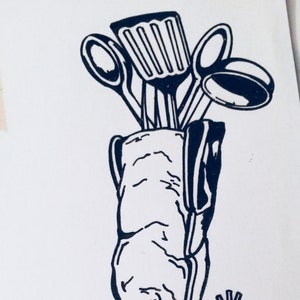 May include: A black and white line drawing of a cowboy boot with a spur. The boot is filled with kitchen utensils, including a spatula, a ladle, and two spoons.
