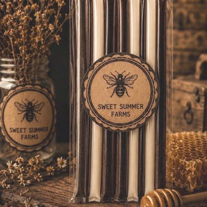 May include: A package of honey sticks from Sweet Summer Farms, with a brown and white striped design. The label features a bee illustration. A jar of dried flowers and a honey dipper are also visible, suggesting a natural product.