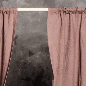 Puede incluir: Un par de cortinas de lino rosa polvoriento colgando de una barra blanca contra una pared gris texturizada. Las cortinas est&aacute;n reunidas en la parte superior y tienen un aspecto relajado y casual. El texto "Wonder Linen" es visible en la esquina inferior derecha de la imagen.