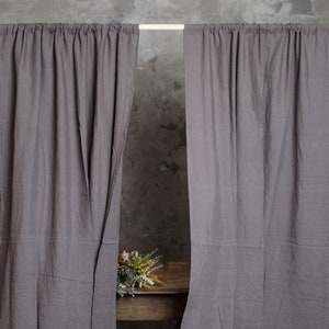 Puede incluir: Dos cortinas de lino gris colgadas de una barra, con un ramo de flores secas sobre una mesa de madera en el fondo. Las cortinas est&aacute;n hechas de una tela suave y natural y tienen una textura sutil. Las cortinas est&aacute;n abiertas, revelando un vistazo a la mesa y las flores.