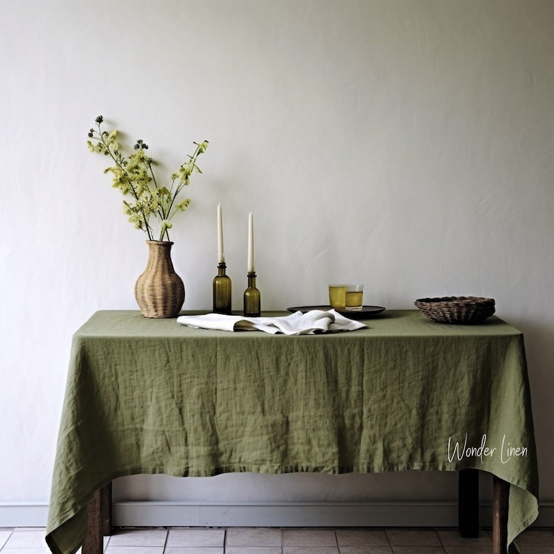 May include: A green linen tablecloth with a woven vase filled with green flowers, two candlesticks with candles, and a small glass of liquid on a wooden table. The text "Wonder Linen" is visible in the bottom right corner of the image.