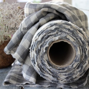 Può includere: Un rotolo di tessuto di lino a quadri grigi e bianchi con bordi sfrangiati. Il tessuto è arrotolato su un tubo di cartone. Il testo "Wonder Linen" è visibile sul tessuto.