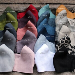 May include: A collection of 20 linen face masks in various colors and patterns, including forest green, moss green, charcoal, gray, light gray, dusty lavender, sky blue, dark blue, white, dusty rose, red, plum, salmon, mint, denim, blue, mustard, natural with black dots, natural with gray stripes, natural, and leopard. The masks are arranged in two rows of ten, with the colors and patterns alternating. The text "Wonder Linen" is visible in the top right corner of the image.
