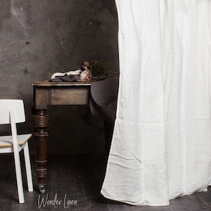 May include: A dark wood table with a white linen tablecloth and a bouquet of dried flowers. The table has turned legs and is set against a grey wall. The table is partially obscured by a white linen curtain.