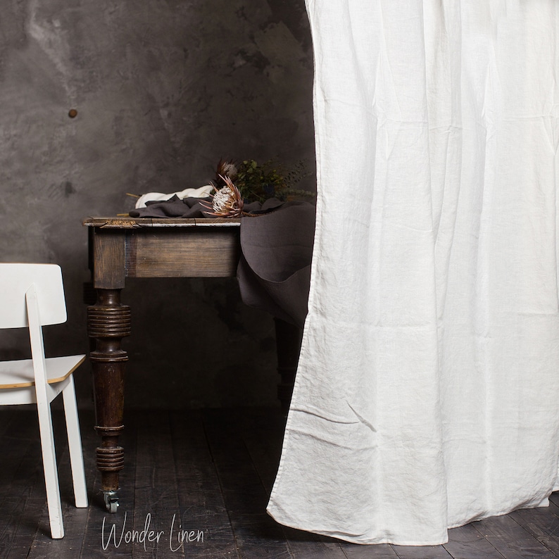 May include: A dark wood table with a white linen tablecloth and a bouquet of dried flowers. The table has turned legs and is set against a grey wall. The table is partially obscured by a white linen curtain.