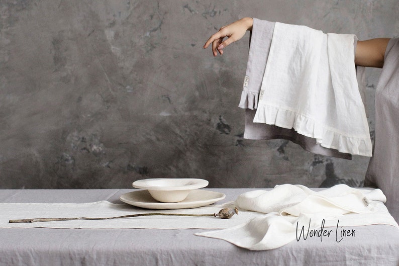 May include: White linen table runner and napkins with a white ceramic bowl and plate on a gray table. The text "Wonder Linen" is visible in the bottom right corner of the image.