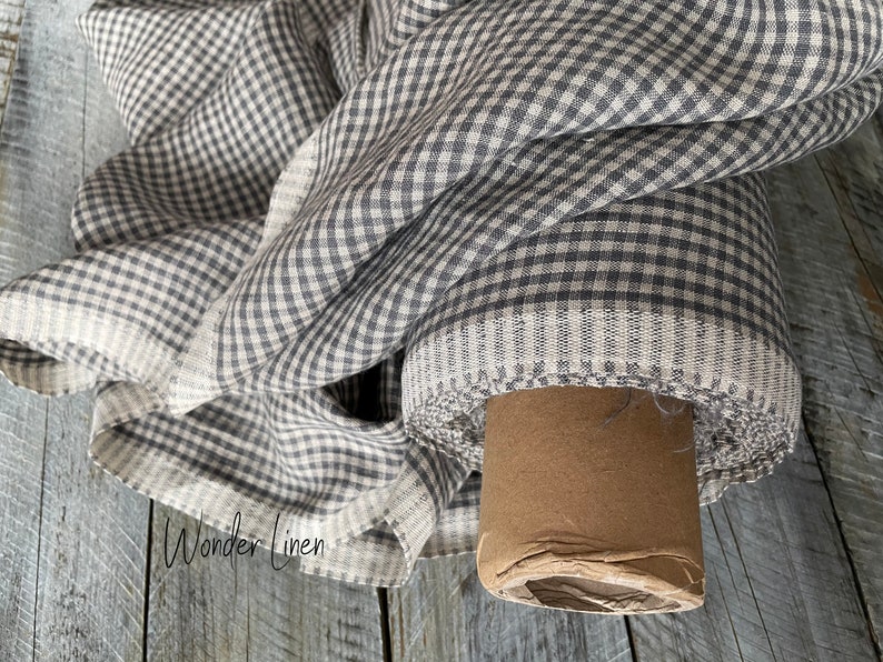 May include: A roll of gray and white gingham linen fabric. The fabric is folded and rolled on a cardboard tube. The fabric has a subtle texture and is perfect for sewing projects.