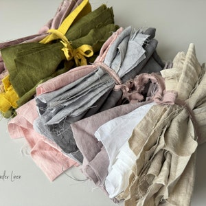 May include: Five bundles of linen fabric in various colors, including green, gray, pink, white, and beige. The fabric is tied together with twine. The text "Wonder Linen" is visible in the bottom left corner of the image.
