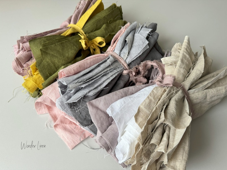 May include: Five bundles of linen fabric in various colors, including green, gray, pink, white, and beige. The fabric is tied together with twine. The text "Wonder Linen" is visible in the bottom left corner of the image.