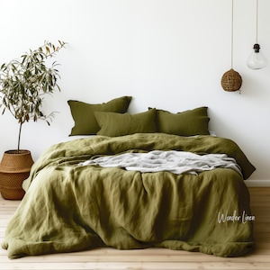 May include: A green linen duvet cover with a matching set of pillowcases. The bedding is on a bed with a white headboard and a wooden floor. The bedding is made by Wonder Linen.