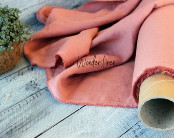 May include: A roll of dusty rose linen fabric with the text "Wonder Linen" printed on it. The fabric is rolled on a cardboard tube and is lying on a light grey wooden surface.