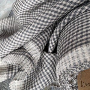 May include: A close-up of a gray and white gingham fabric. The fabric is folded and has a soft, textured feel. The fabric is made of linen and is perfect for sewing projects.