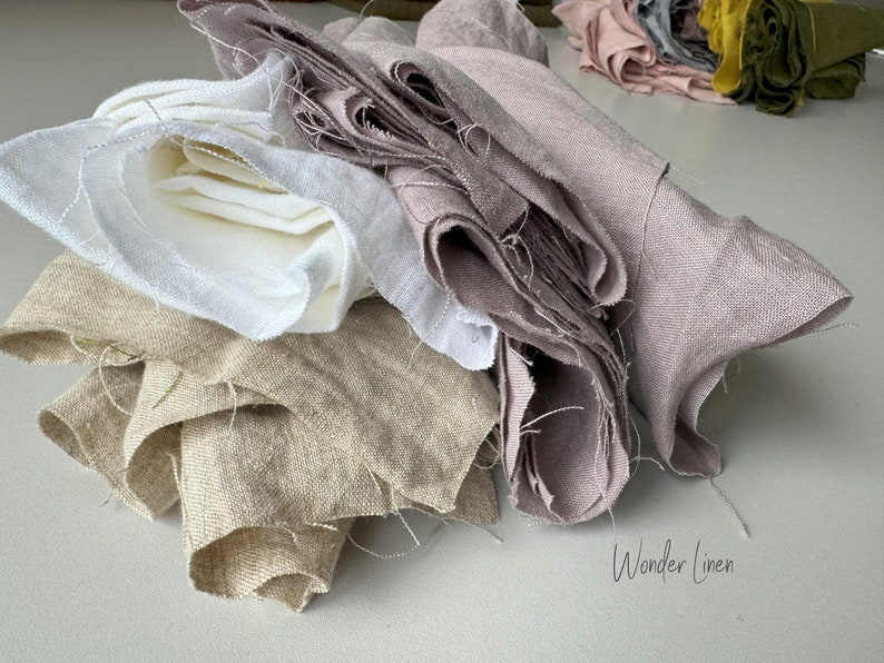 May include: A stack of four different colored linen fabrics. The fabrics are folded and arranged in a pile. The colors are white, beige, light brown, and light pink. The text "Wonder Linen" is visible at the bottom of the image.