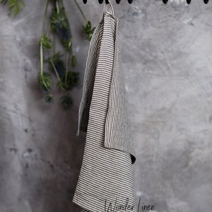 K&ouml;nnte beinhalten: Ein gestreiftes Leinen-Geschirrtuch, das an einem Gestell h&auml;ngt. Das Tuch ist hellbeige mit dunkelgrauen Streifen. Auf dem Tuch steht "Wonder Linen" gedruckt.