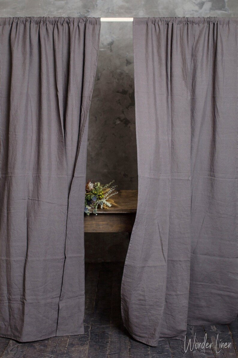 Puede incluir: Dos cortinas de lino gris colgadas de una barra, con un ramo de flores secas sobre una mesa de madera en el fondo. Las cortinas est&aacute;n hechas de una tela suave y natural y tienen una textura sutil. Las cortinas est&aacute;n abiertas, revelando un vistazo a la mesa y las flores.