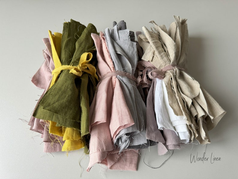 May include: Four bundles of linen fabric in various colors, including green, pink, gray, and beige. The fabric is tied together with twine and arranged on a white surface. The text "Wonder Linen" is visible in the bottom right corner of the image.