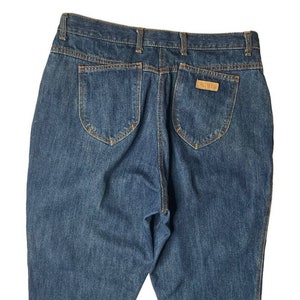 Può includere: Un paio di jeans blu denim con una toppa in pelle marrone sulla tasca posteriore che dice "GANT"