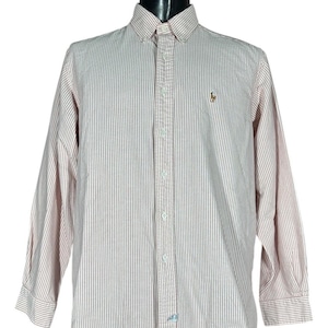 May include: A button-down shirt with vertical red and white stripes. The long-sleeved shirt features a button-down collar and a small embroidered logo on the chest. The shirt has a classic fit and is made of a lightweight fabric.