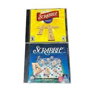 May include: Two Scrabble PC game cases stacked vertically. The top case is yellow with the title Scrabble Champion Edition and wooden tiles spelling Family Night. The bottom case is blue with the Scrabble logo and floating wooden letter tiles.