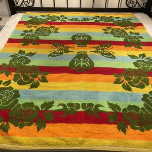 May include: A colorful striped throw blanket with a floral design featuring green roses and butterflies. The blanket has a red, orange, yellow, green, and blue striped pattern.
