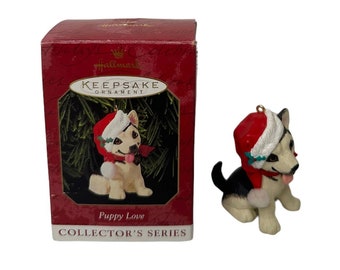 Könnte beinhalten: Hallmark Keepsake Ornament mit einem Welpen, der einen Weihnachtsmannhut und einen Schal trägt. Der Welpe ist schwarz, weiß und hellbraun, mit herausgestreckter Zunge. Das Ornament stammt aus der "Puppy Love" Collector's Series.