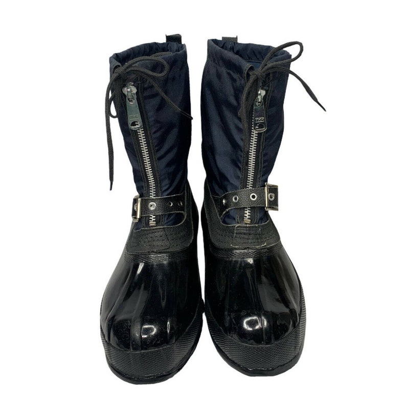 K&ouml;nnte beinhalten: Ein Paar schwarze und marineblaue Winterstiefel mit einem Rei&szlig;verschluss vorne und einem Schnallenriemen. Die Stiefel haben eine gl&auml;nzende schwarze Gummisohle.