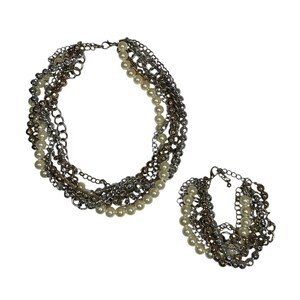 Puede incluir: Un conjunto de collar y pulsera de varias hebras. El collar y la pulsera presentan capas de cadenas plateadas y perlas de imitación. El conjunto de joyas se muestra sobre un fondo blanco.