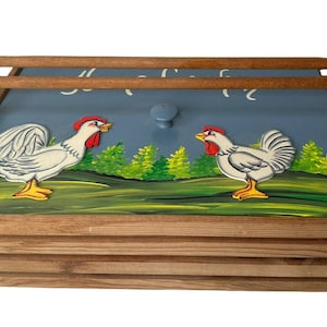 May include: A wooden bread bin with a blue lid and a painted scene of two white chickens on a green field. The lid has a wooden handle and the words "Il Fait Bon" are painted on the lid.