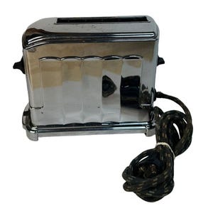 Puede incluir: Una tostadora vintage cromada con un cable negro. La tostadora tiene un diseño acanalado y una forma redondeada.