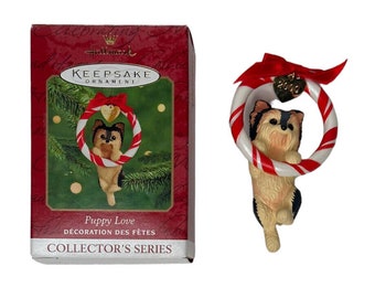 Può includere: Un ornamento natalizio della serie da collezione Hallmark Keepsake Ornament che presenta un piccolo cane marrone e nero che tiene una ghirlanda di bastoncini di zucchero. L'ornamento è etichettato "Puppy Love" e "Décoration des Fêtes".