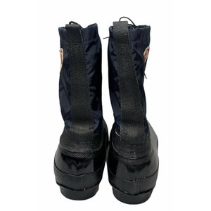 K&ouml;nnte beinhalten: Ein Paar schwarze Gummistiefel mit einem dunkelblauen Nylon-Obermaterial. Die Stiefel haben eine schwarze Lasche an der R&uuml;ckseite und ein rotes Logo an der Seite.