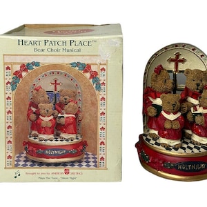 Puede incluir: Una figura musical navideña con un grupo de osos vestidos con túnicas rojas cantando en un escenario de iglesia. La figura reproduce la melodía "Noche de Paz".