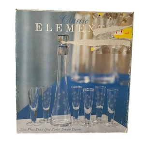 May include: A box containing a seven-piece etched glass cordial set with a decanter. The box is labeled "Classic Elements" and features a photo of the set. The glasses and decanter are clear and have a starburst design.