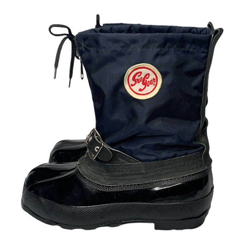 K&ouml;nnte beinhalten: Schwarze Gummistiefel mit einem dunkelblauen Nylon-Obermaterial und einer schwarzen Schnalle. Die Stiefel haben ein wei&szlig;es Etikett mit dem Text "Sno-Goer" in Rot.