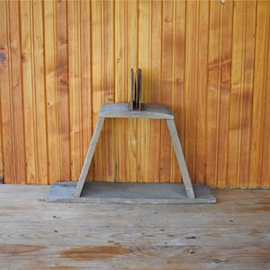 Puede incluir: Una estantería de madera rústica de dos niveles, hecha de madera recuperada. La estantería está sostenida por dos patas inclinadas y tiene un acabado de madera natural.