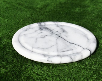 May include: A white marble round coaster with a slightly raised edge. The coaster has a natural veining pattern.
