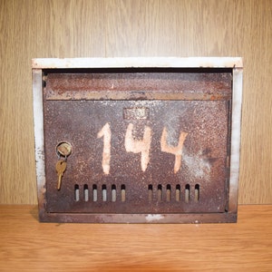May include: A rusty metal mailbox with the number "144" painted in white on the front. The mailbox has a keyhole and a small key in it.