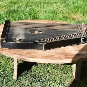 Può includere: Uno ziter in legno nero con denti di metallo si trova su un tavolo rotondo in legno con tre gambe. Il tavolo è su una superficie erbosa.