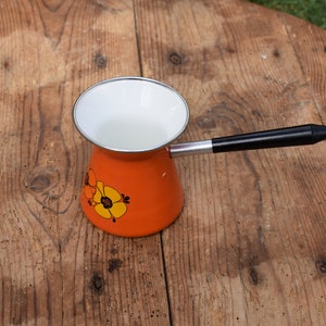 May include: Orange and white enamel coffee pot with a black handle and floral design.