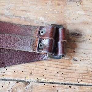May include: Close-up of a brown leather belt with a metal buckle. The belt is folded in half and the buckle is closed.