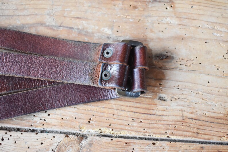 May include: Close-up of a brown leather belt with a metal buckle. The belt is folded in half and the buckle is closed.