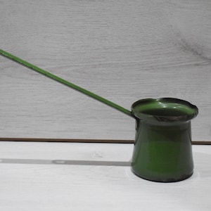 May include: A green metal coffee pot with a long handle. The pot has a slightly rounded shape and a slightly flared lip.