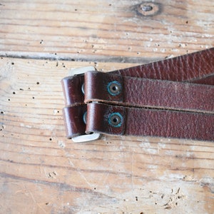May include: Close-up of a brown leather strap with two silver buckles and turquoise accents. The strap is folded in half and the buckles are closed.