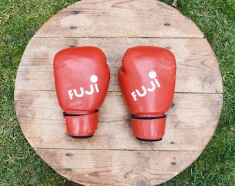May include: Two red boxing gloves with white "FUJI" branding on a wooden surface.