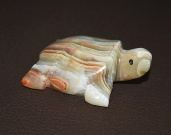 May include: A small, carved turtle figurine made of green, brown, and white onyx. The turtle has a black eye and is lying on its belly.