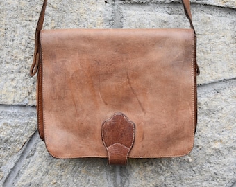 May include: A brown leather messenger bag with a flap closure and a decorative leather accent on the front.